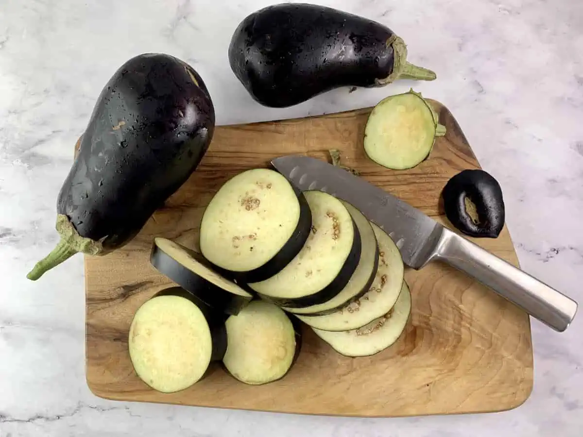 CUTTING EGGPLANTS INTO ROUNDS WITH A KNIFE ON A WOODEN BOARD