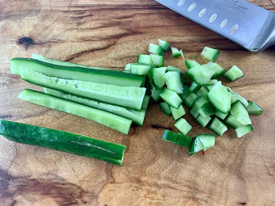 Finely dicing cucumber on a wooden board with a knife on the side.