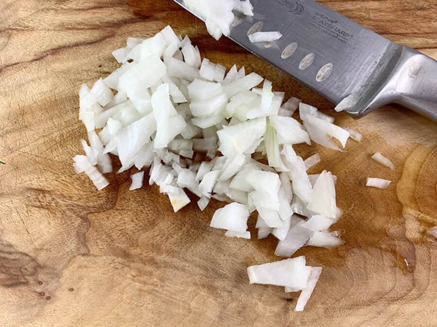 Onion cut in a small dice on a wooden board with a knife on the side.