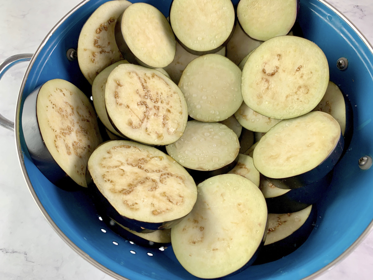 Salted eggplant rounds in a colander with water beads forming.