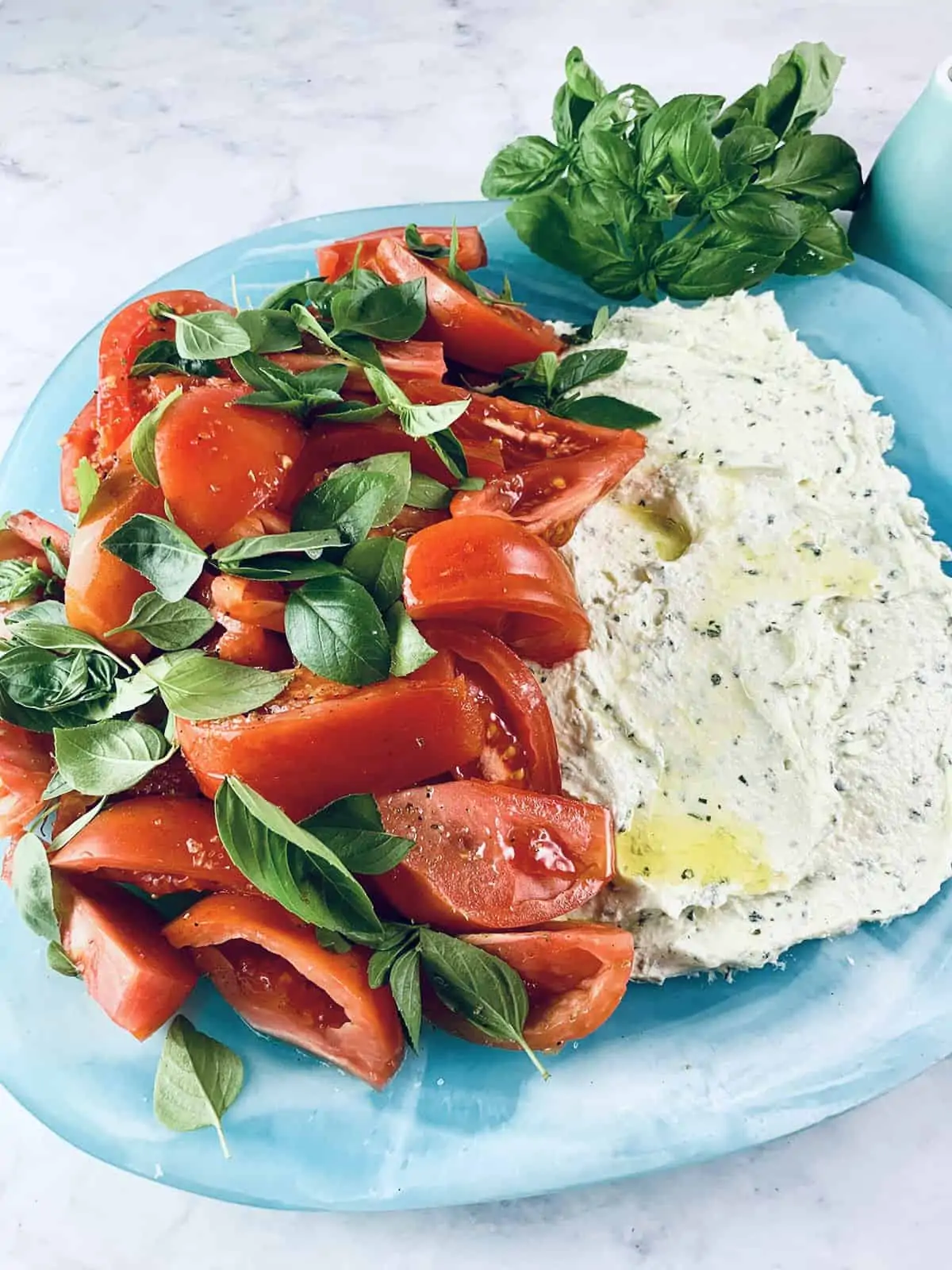 Heirloom tomato and whipped feta salad on a aqua platter with basil sprigs and oil on the side.