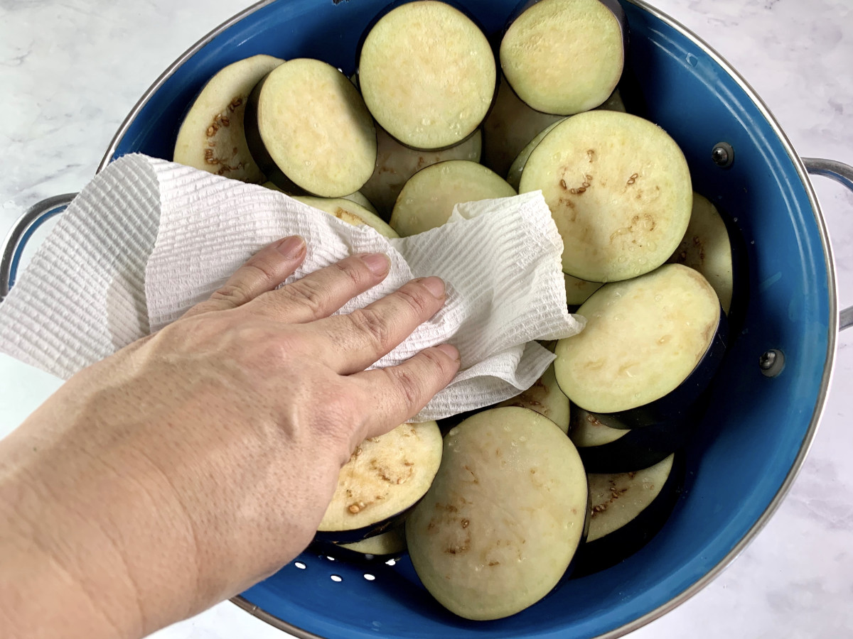 PATTING EGGPLANT ROUNDS IN A COLANDER TO REMOVE WATER BEADS