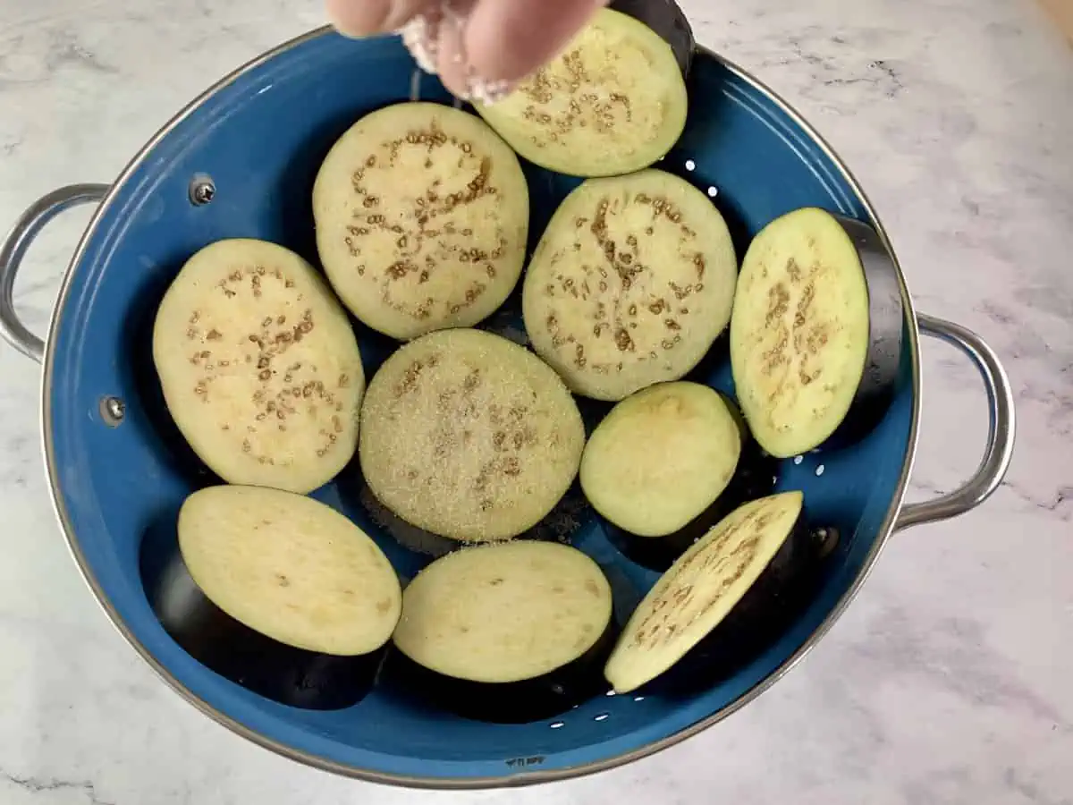 SALTING EGGPLANT ROUNDS 1 LAYER AT A TIME IN A COLANDER