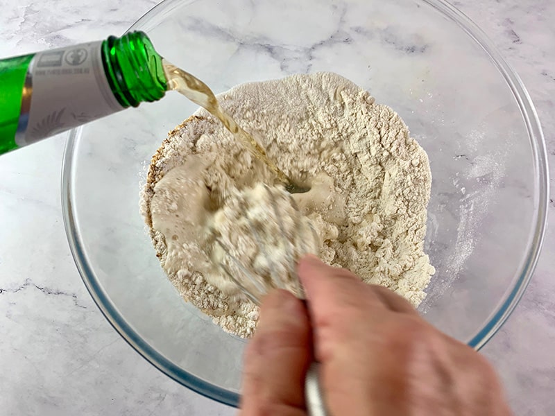 Hands pouring bear into dry batter ingredients.