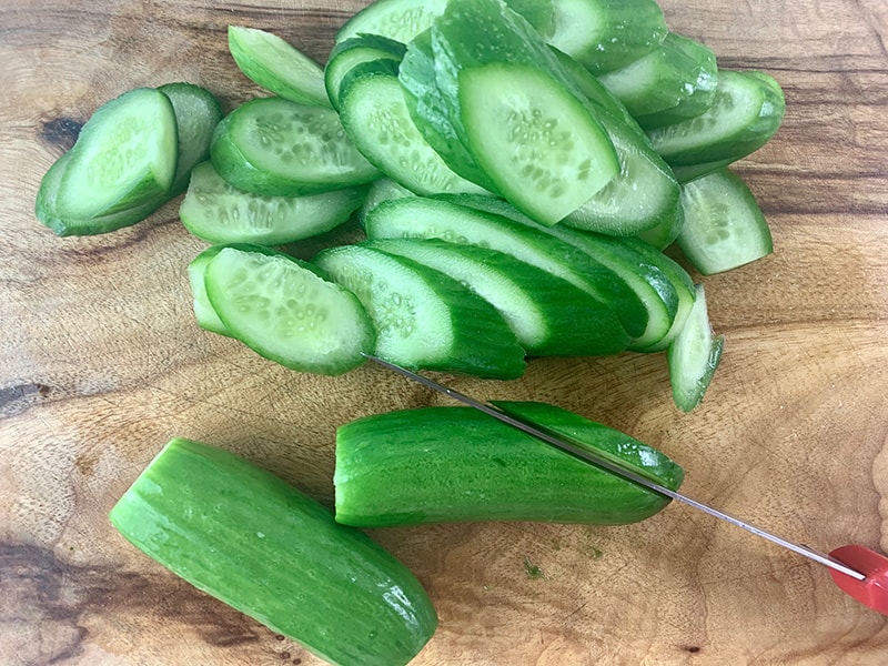 Slicing quks or cukes on the diagonal with a knife on a wooden board.