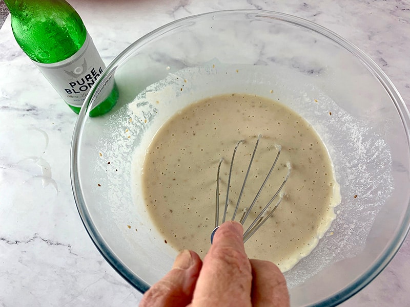 Mixing beer batter with a whisk in a glass bowl.