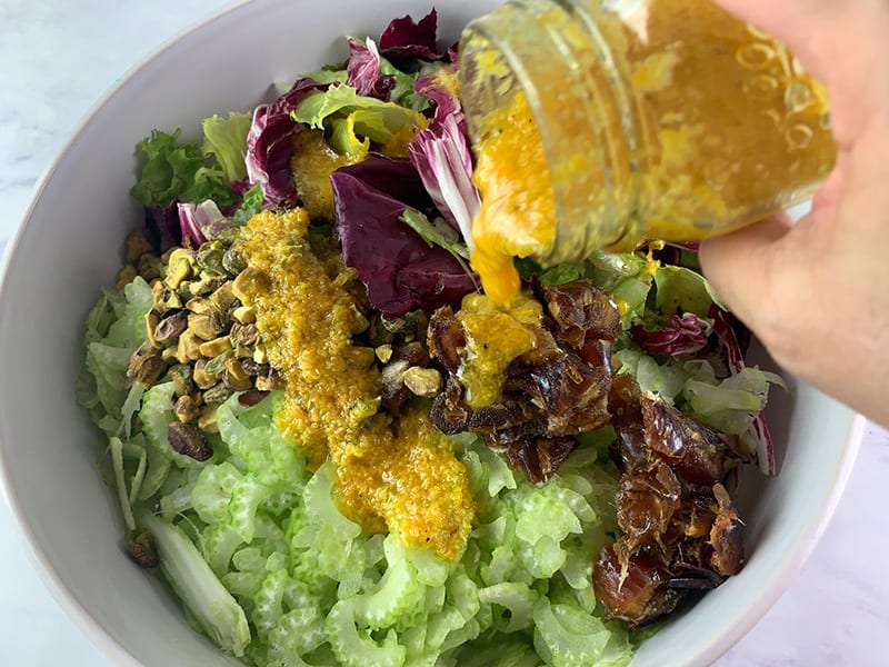 POURING TURMERIC DRESSING OVER GREEN SALAD