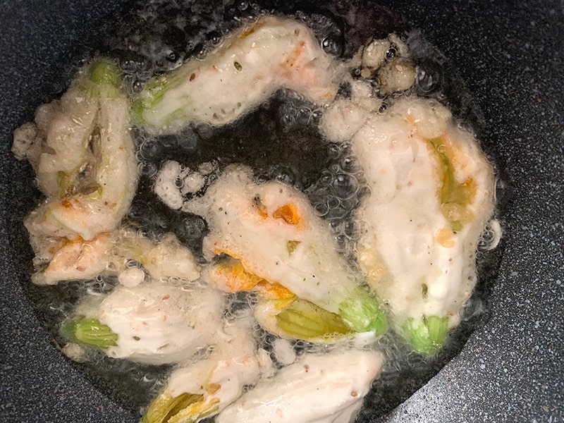 Battered zucchini flowers frying in hot oil.