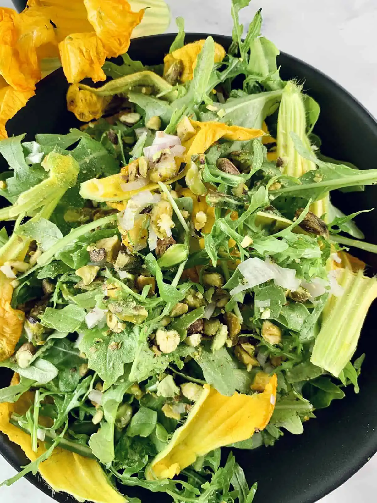Close-up of arugula salad with squash flowers with zucchini flowers on the side.