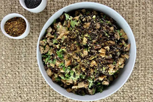 Wild rice salad in a white bowl with furikake and black sesame seeds in small white bowls on the side.