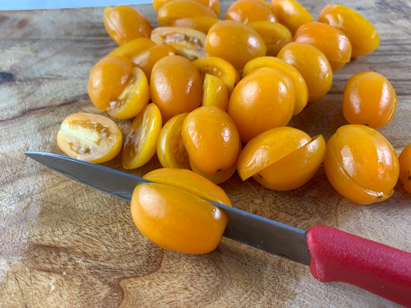 CLOSE UP OF CUTTING MINI ROMA/OVAL TOMATOES IN HALF