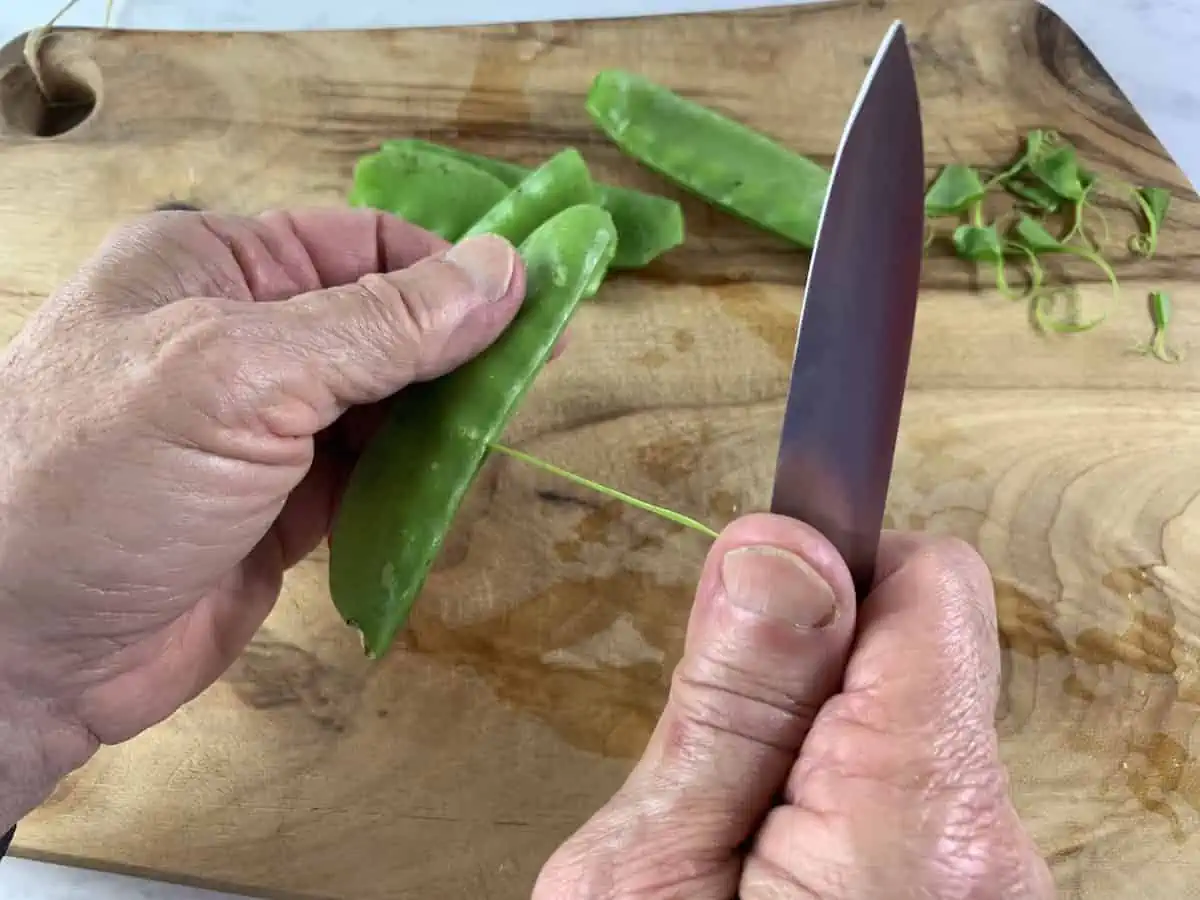 Hands stringing snow peas over a wooden board.