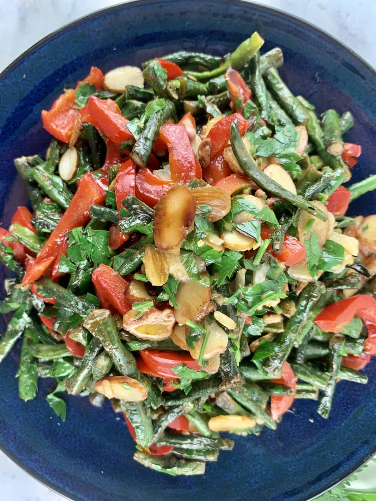 A close-up of Snake Bean Salad with Red Peppers and Almonds on a blue plate.