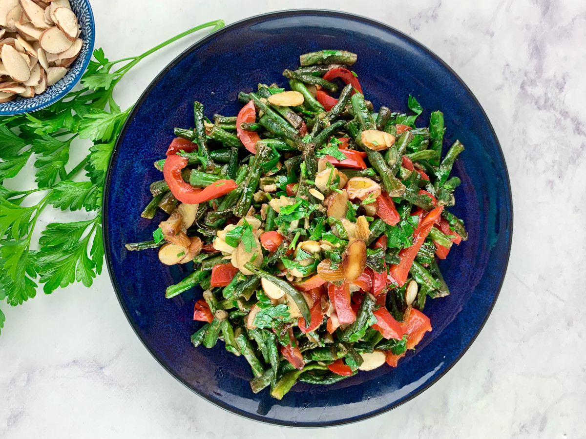Snake Bean Salad with Red Peppers and Almonds on a blue plate with parsley sprig and bowl of almonds on the side.