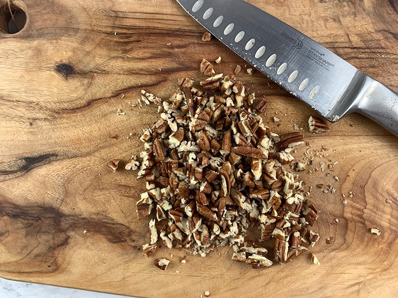 CHOPPING PECANS ON WOODEN BOARD WITH KNIFE