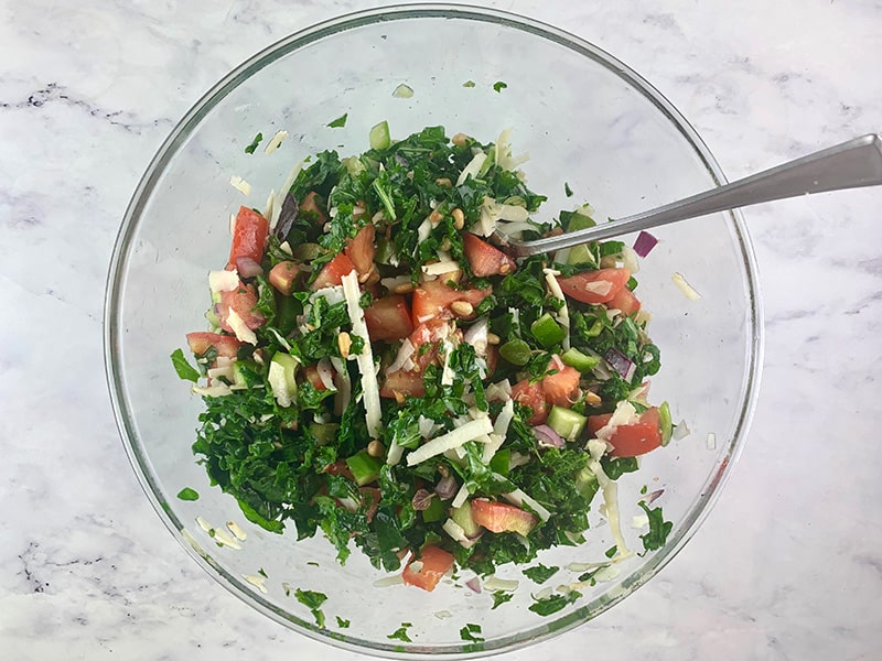 MIXING CHOPPED KALE SALAD IN A BOWL WITH A SPOON