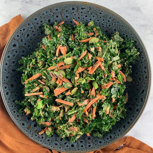 Kale and broccoli salad in a ceramic bowl with an orange linen napkin on the side.