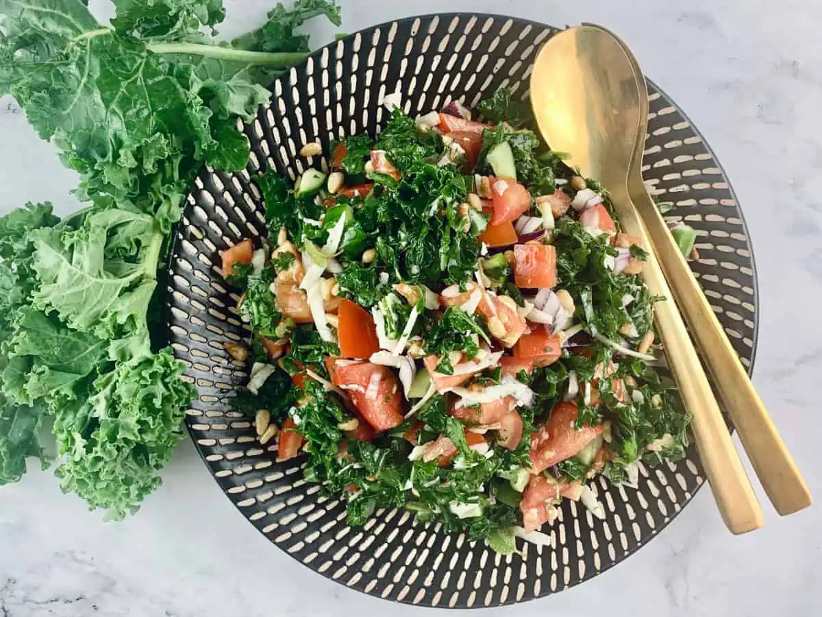 Kale chopped salad in a patterned plate with gold serves and kale leaves on the side.