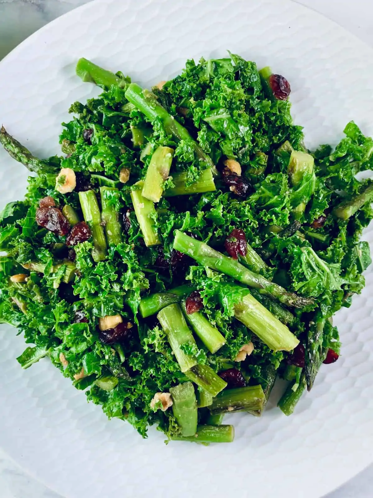A close-up of Kale and Cranberry Salad on a white patterned plate with curly kale in top left corner.