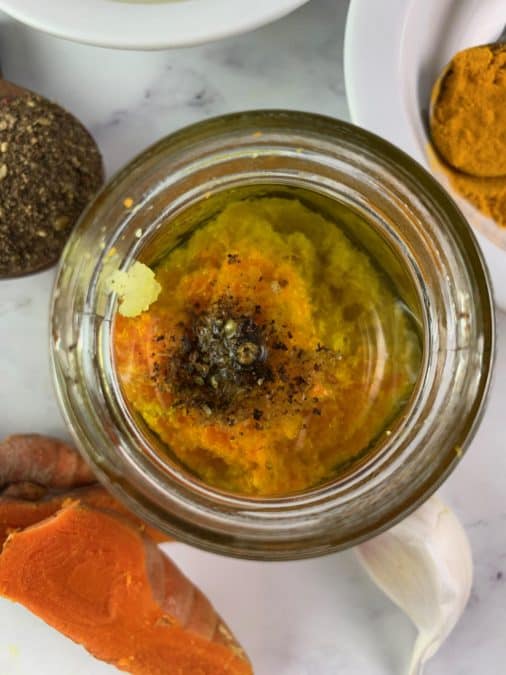 OVERHEAD VIEW OF TURMERIC DRESSING INGREDIENTS IN A GLASS JAR WITH FRESH TURMERIC, GARLIC AND SALT AND PEPPER ON THE SIDE