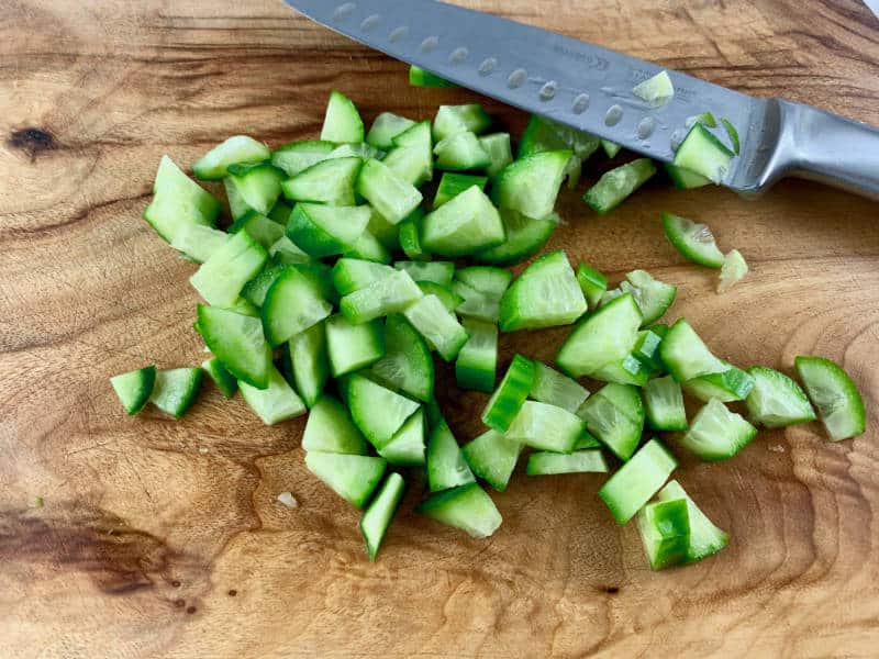DICING CUCUMBER ON A WOODEN BOARD WITH A KNIFE