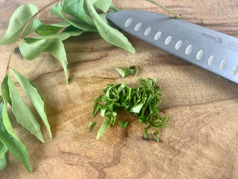 CUTTING CURRY LEAVES ON A WOODEN BOARD WITH A KNIFE