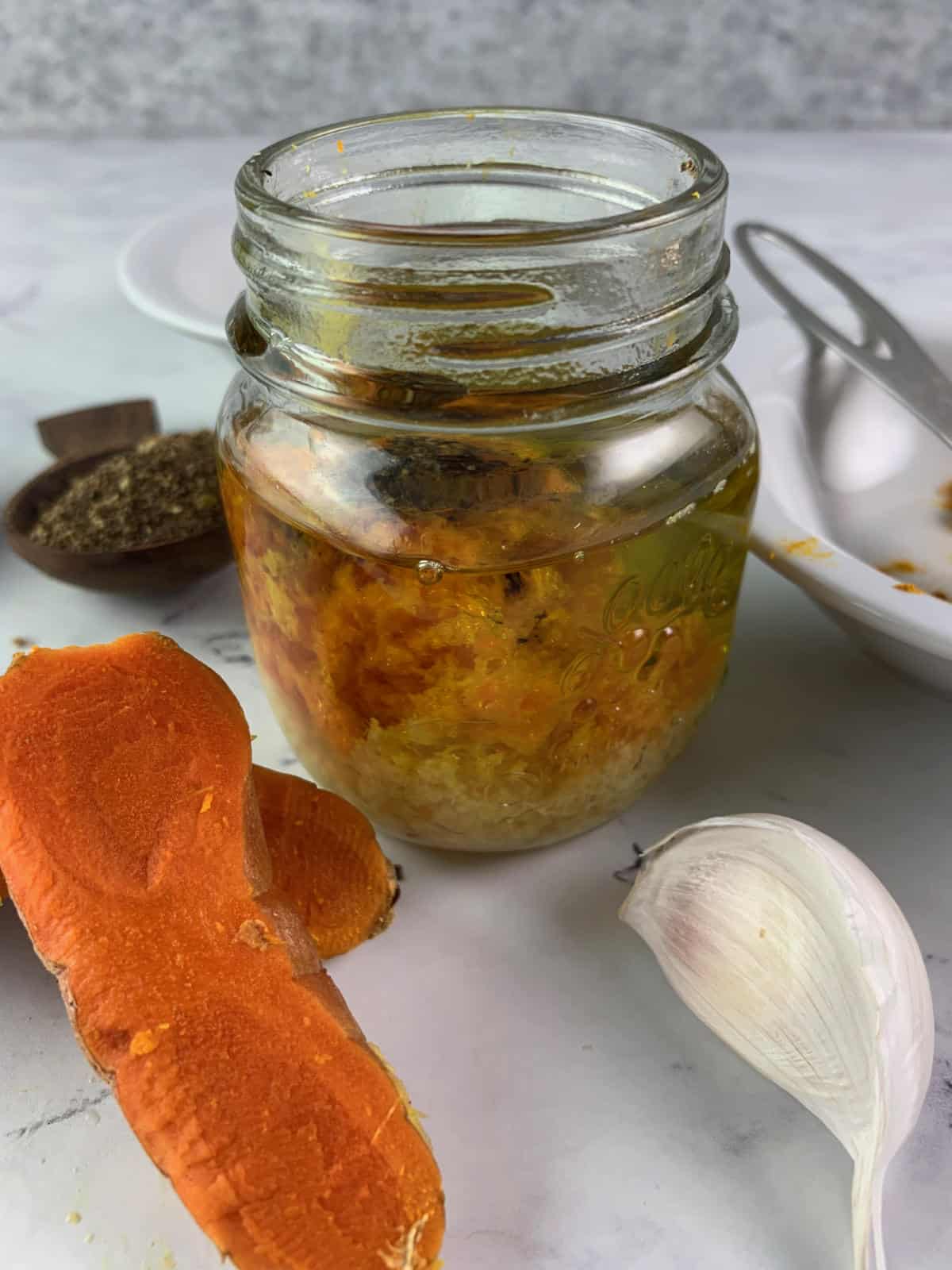 TUMERIC DRESSING INGREDIENTS IN A GLASS JAR WITH FRESH TURMERIC & GARLIC ON THE SIDE
