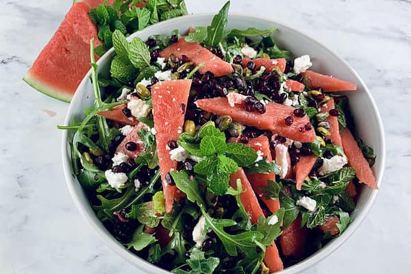 Persian watermelon & feta salad in a white bowl with watermelon slices & mint on the side.