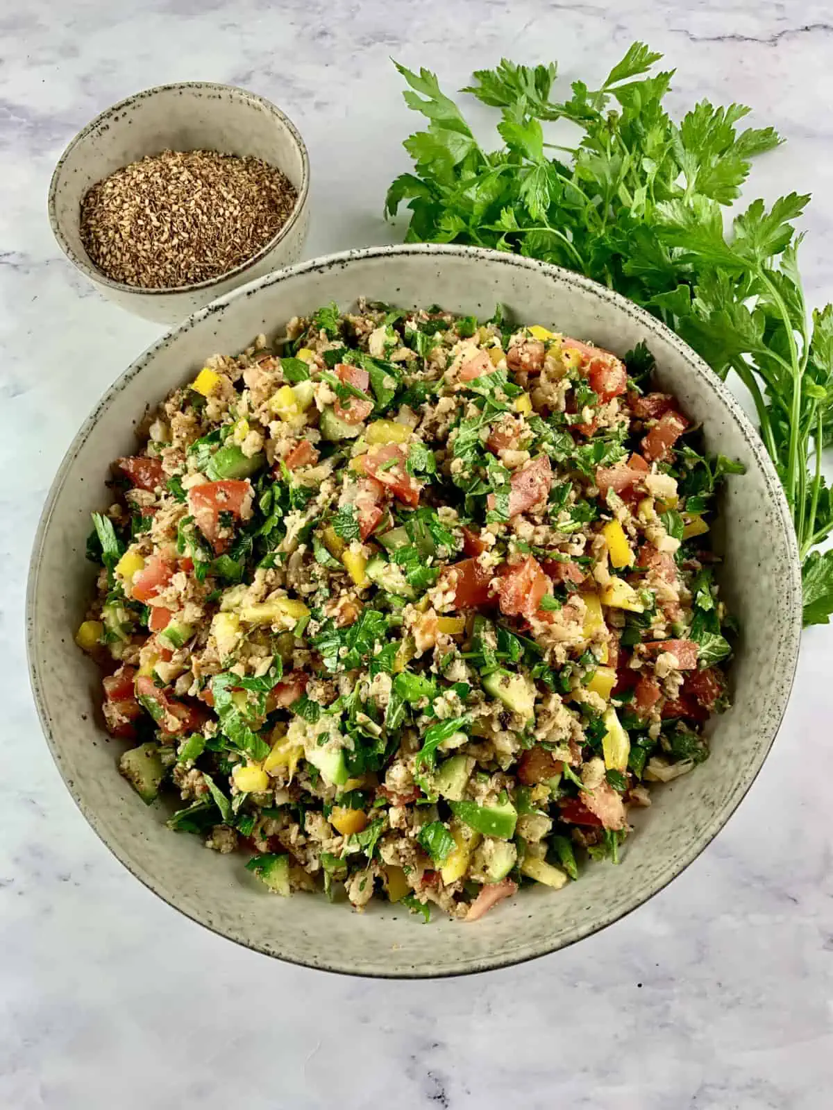 Cauliflower tabbouleh in a bowl with za'atar and parsley on the side.