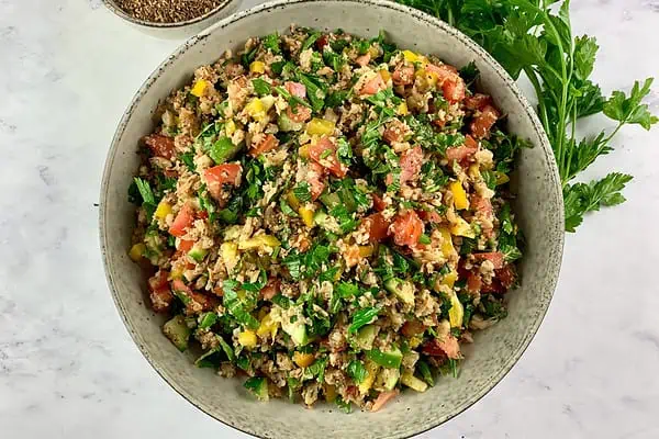 Cauliflower tabbouleh in a bowl with za'atar and parsley on the side.