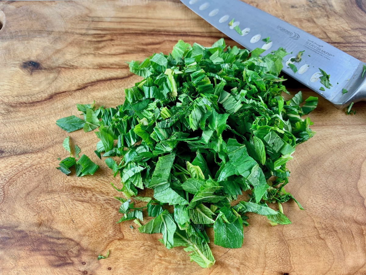 Chopping mint leaves on a wooden board with a knife.