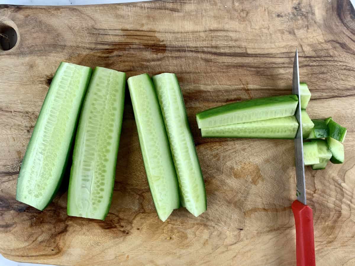 CUTTING CUCUMBERS ON A WOODEN BOARD WITH A KNIFE
