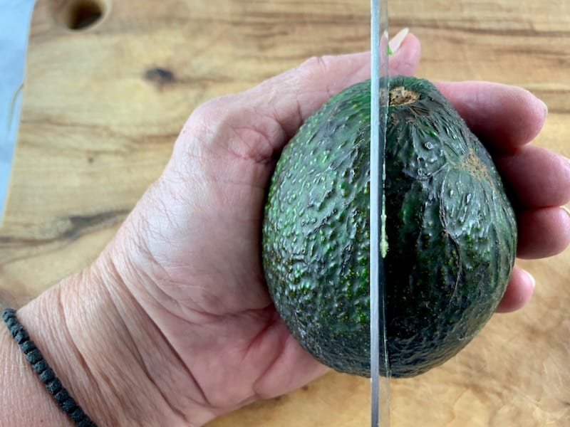 SLICING AROUND AN AVOCADO WITH A KNIFE ON A WOODEN BOARD