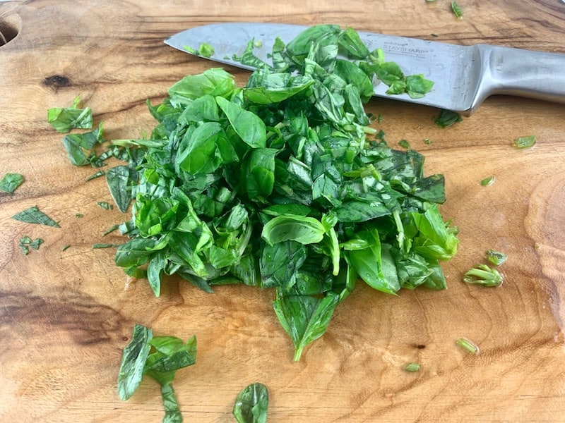 CHOPPING BASIL ON WOODEN BOARD WITH A KNIFE
