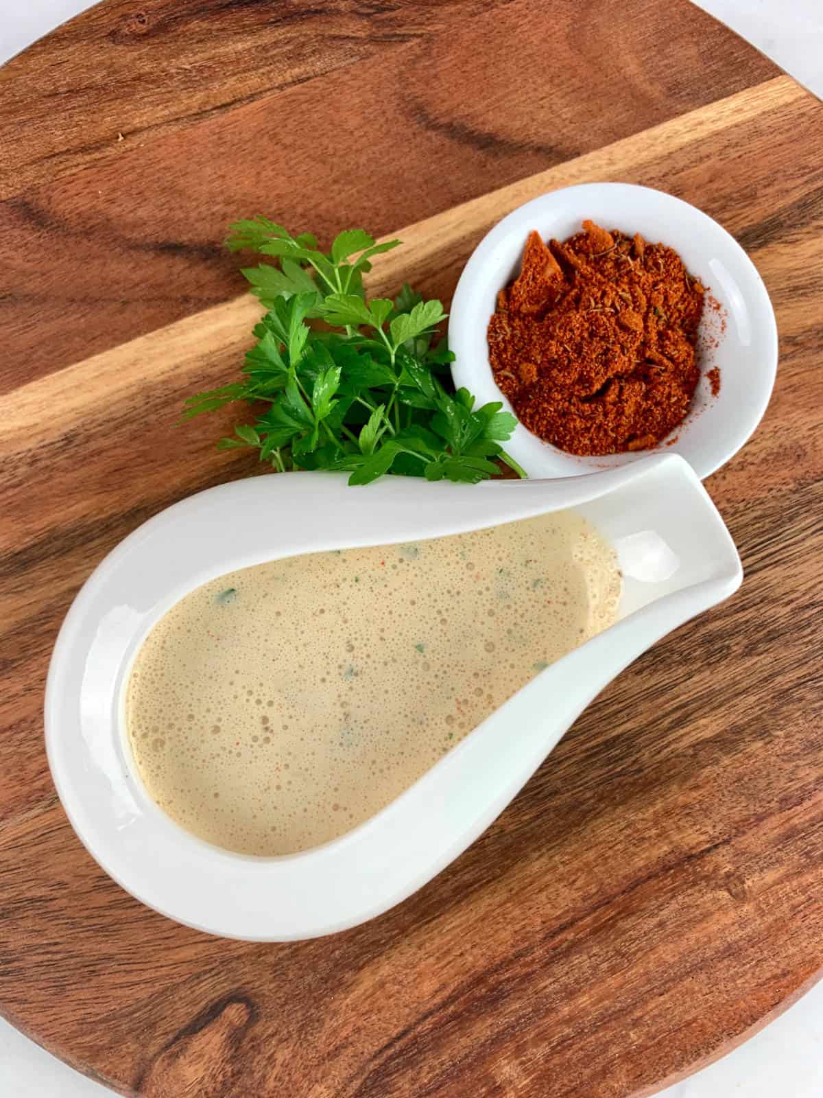 CAJUN SALAD DRESSING IN A WHITE BOWL WITH CAJUN SPICE & PARSLEY GARNISH ON A WOODEN BOARD