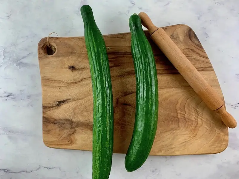 LONG TELEGRAPH CUCUMBERS ON WOODEN BOARD WITH ROLLING PIN