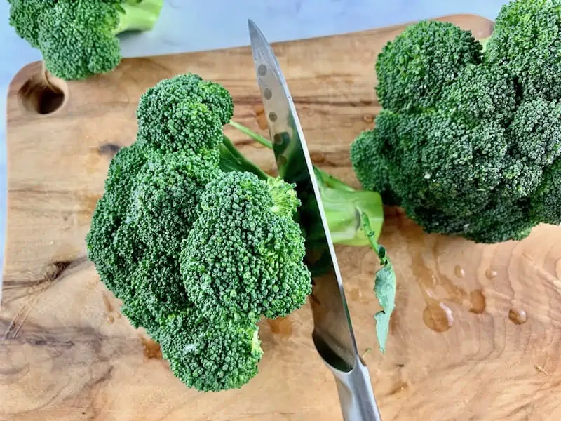 CUTTING OFF BROCCOLI STEMS WITH A KNIFE ON WOODEN BOARD