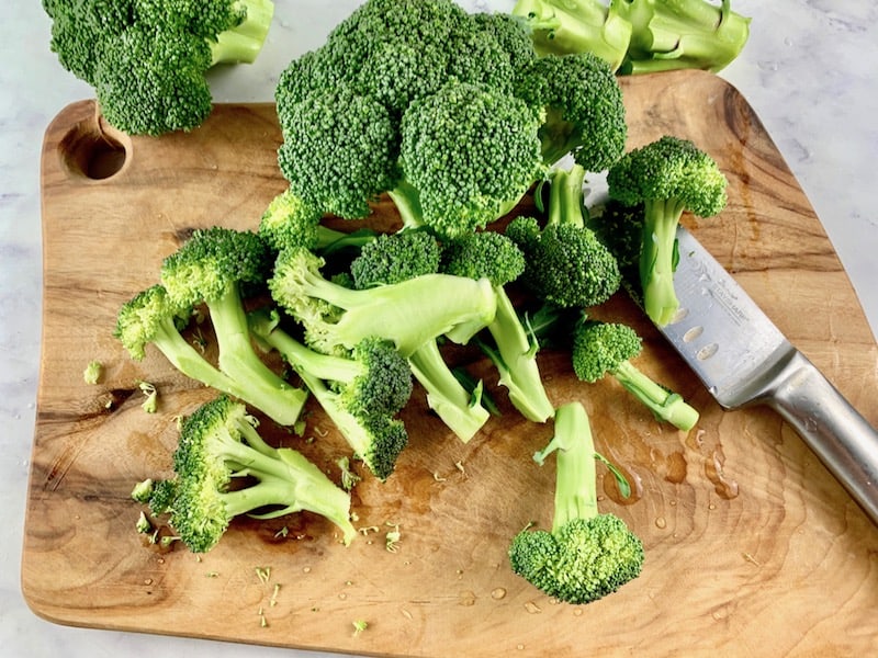 CUTTING BROCCOLI INTO FLORETS ON WOODEN BOARD WITH KNIFE