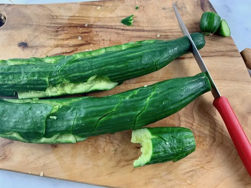 RIMMING SMASHED CUCUMBERS WITH A KNIFE ON A CHOPPING BOARD