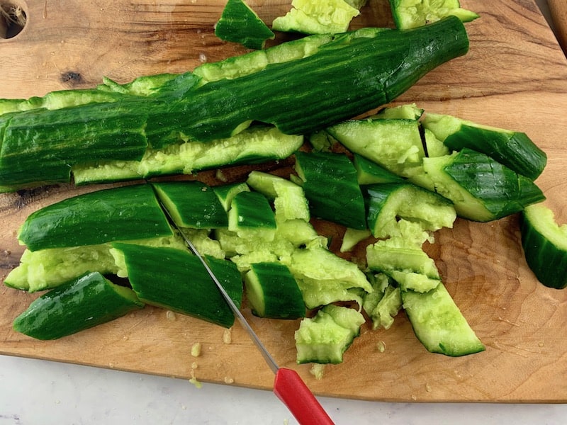 CUTTING SMASHED CUCUMBERS WITH A KNIFE ON A WOODEN BOARD