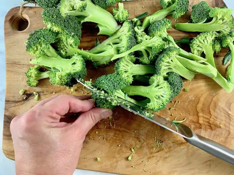 SLICING BROCCOLI FLORETS IN HALF WITH KNIFE ON WOODEN BOARD