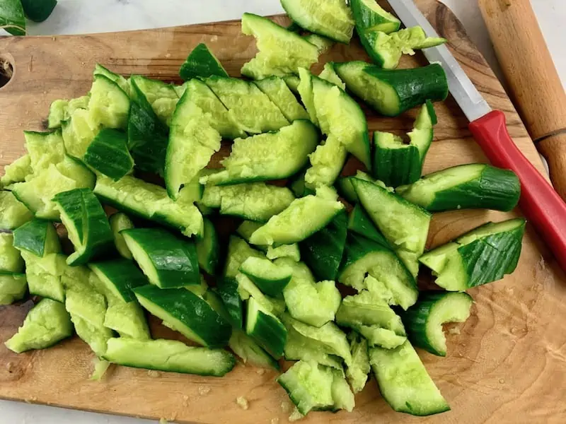 CUT SMASHED CUCUMBERS WITH KNIFE ON WOODEN BOARD