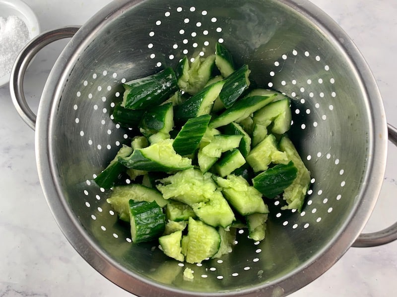 TOSSING THE CUCUMBERS IN SALT IN A COLANDER