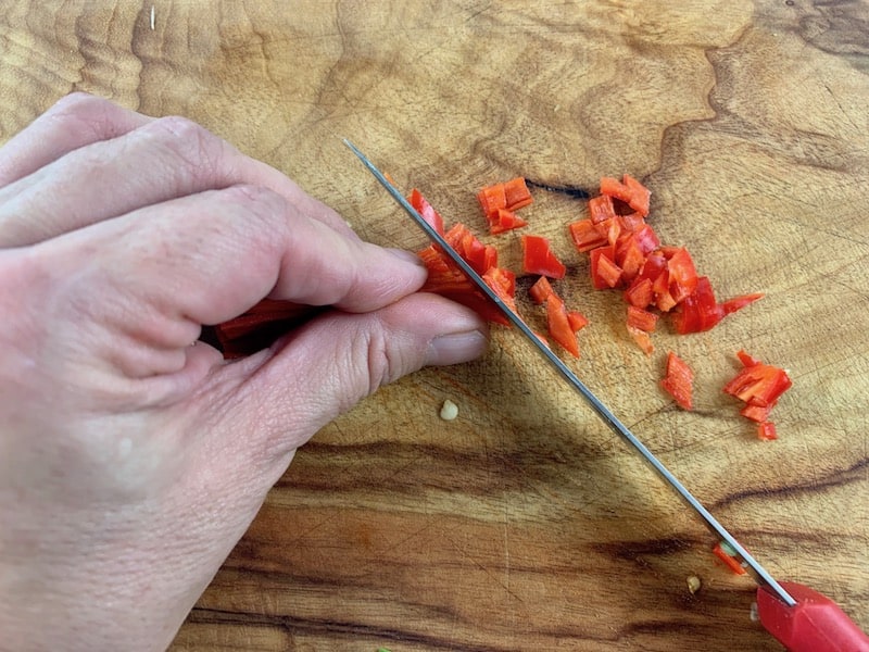 DICING RED CHILLI ON A WOODEN BOARD WITH RED KNIFE