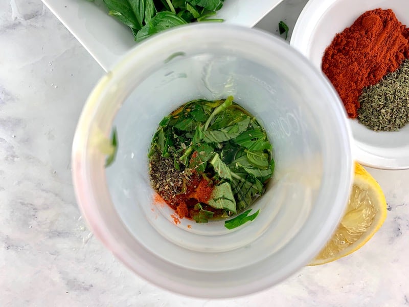 ITALIAN VINAIGRETTE INGREDIENTS IN A BLENDER WITH BASIL AND HERBS IN BACKGROUND