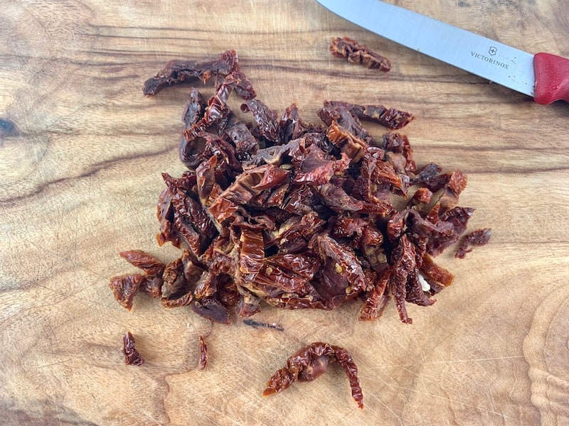 CUTTING DRIED TOMATOES INTO STRIPS ON WOODEN BOARD