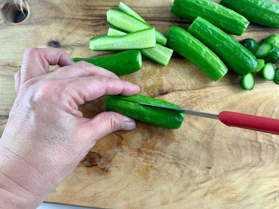 SLICING CUKES IN HALF ON WOODEN BOARD WITH RED KNIFE