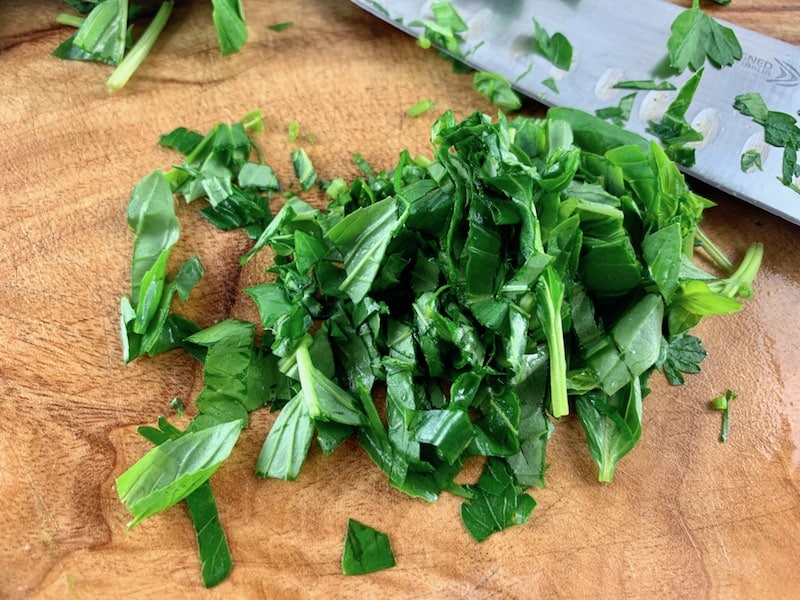 Roughly chopping basil leaves on a wooden board with a knife.