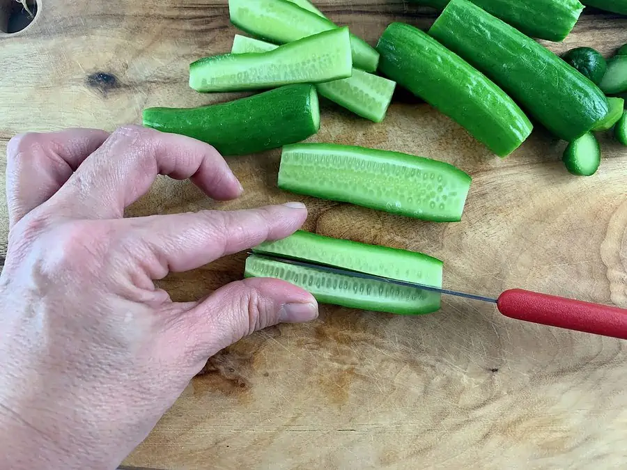 SLICING CUKES IN QUARTERS ON WOODEN BOARD WITH RED KNIFE