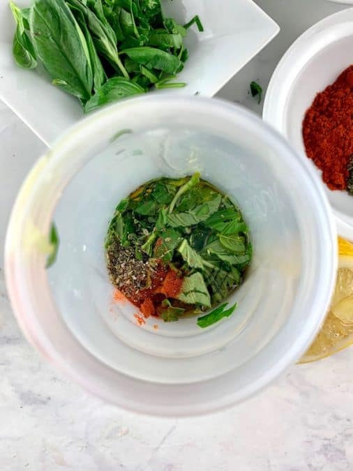 Italian vinaigrette ingredients in a blender with basil and herbs in background.